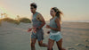a fit couple running down the beach during a sunset